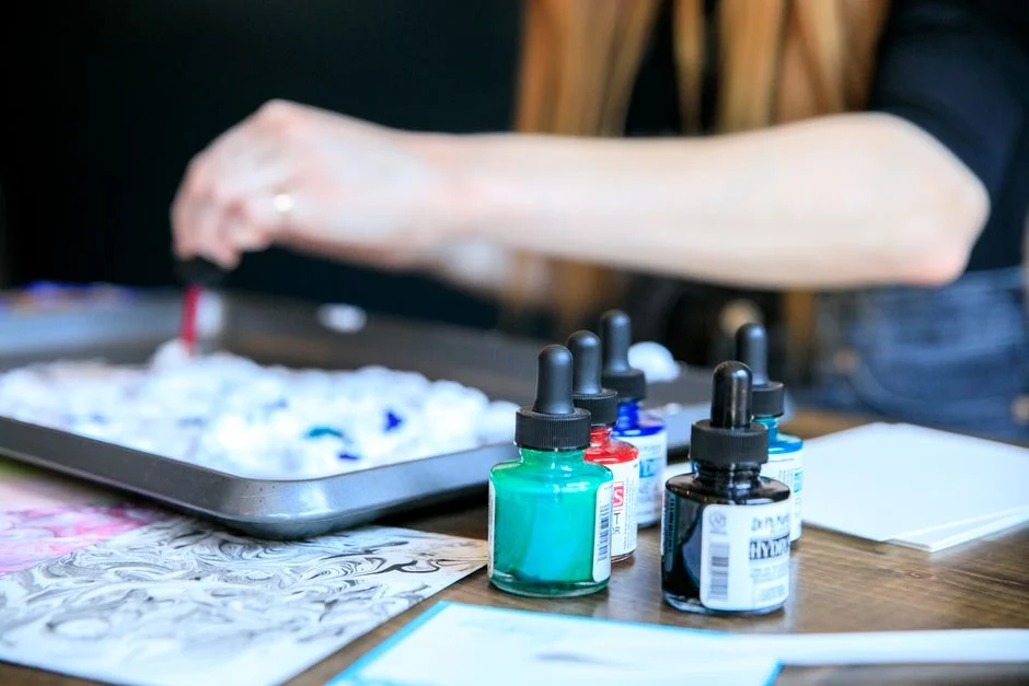 Artist using ink bottles and shaving foam for marbling art. Hands and materials in focus.